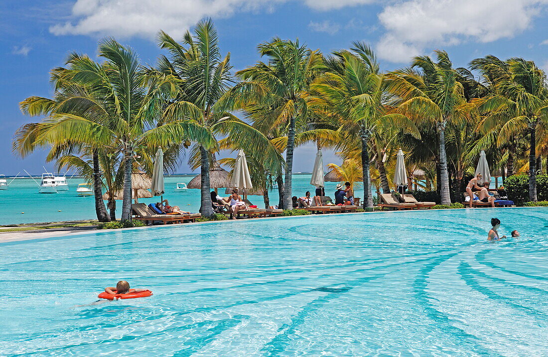 People and palm trees at the pool of Beachcomber Hotel Paradis &amp; Golf Club, Mauritius, Africa