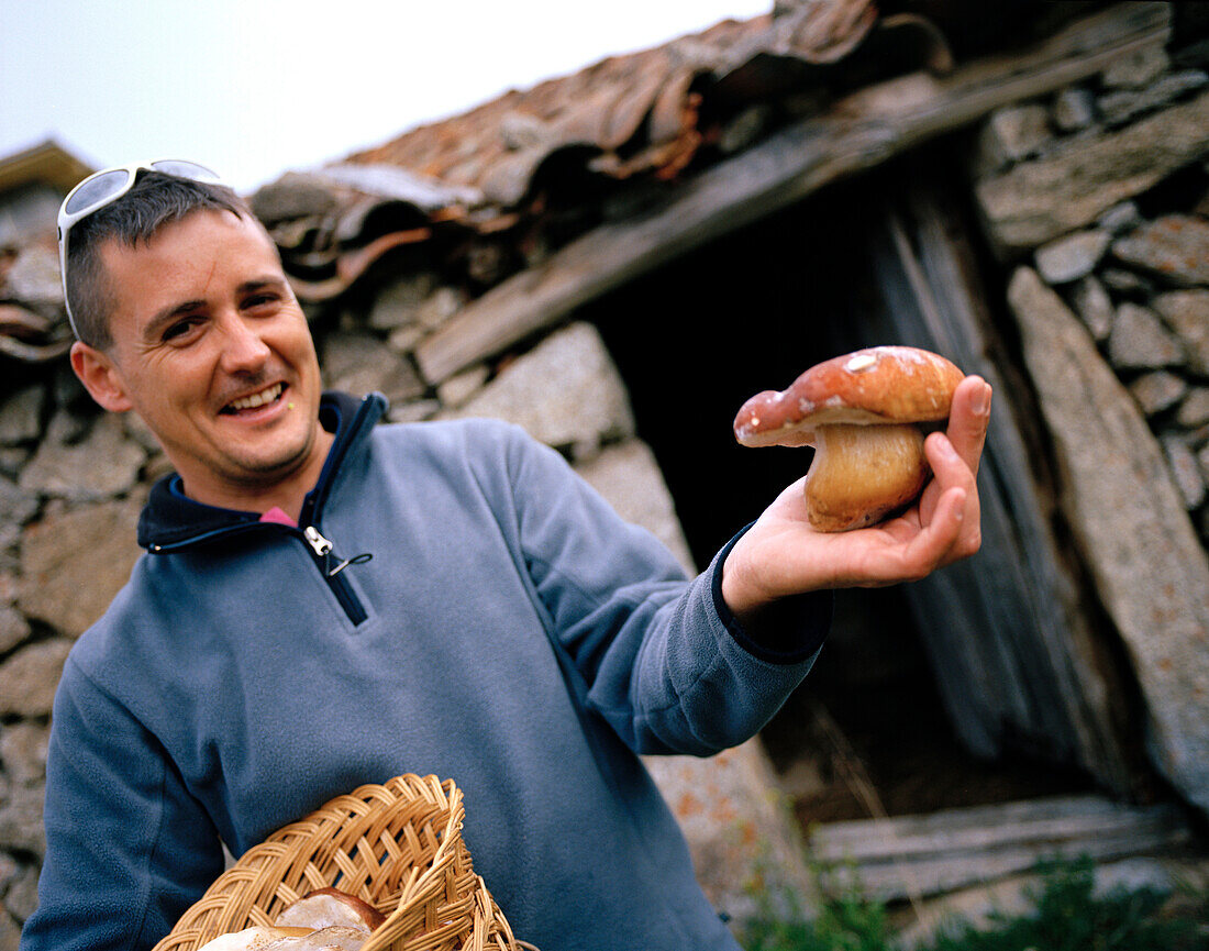 Nature guide, gredos guides, holding a boletus pinophilus, pine bolete, in front of an old stone house, San Martin del Pimpollar, Sierra de Gredos, Castile and Leon, Spain
