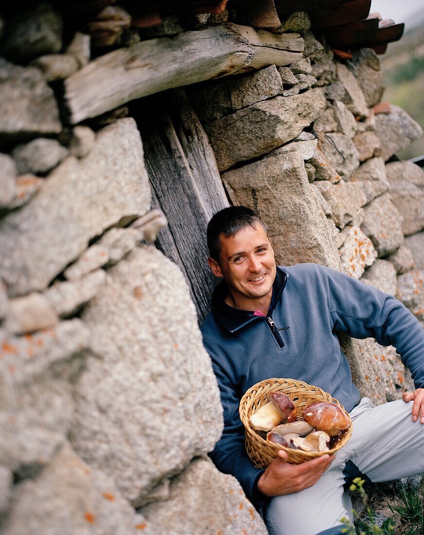 Nature guide (gredos guides) with boletus pinophilus, pine bolete, in front of an old stone house, San Martin del Pimpollar, Sierra de Gredos, Castile and Leon, Spain