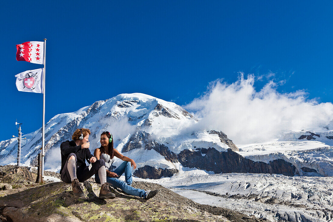 Zwei junge Leute mit Kopfhörern sitzen auf einem Stein, Klimahörpfad von myclimate, Neue Monte-Rosa-Hütte, Zermatt, Walliser Alpen, Kanton Wallis, Schweiz