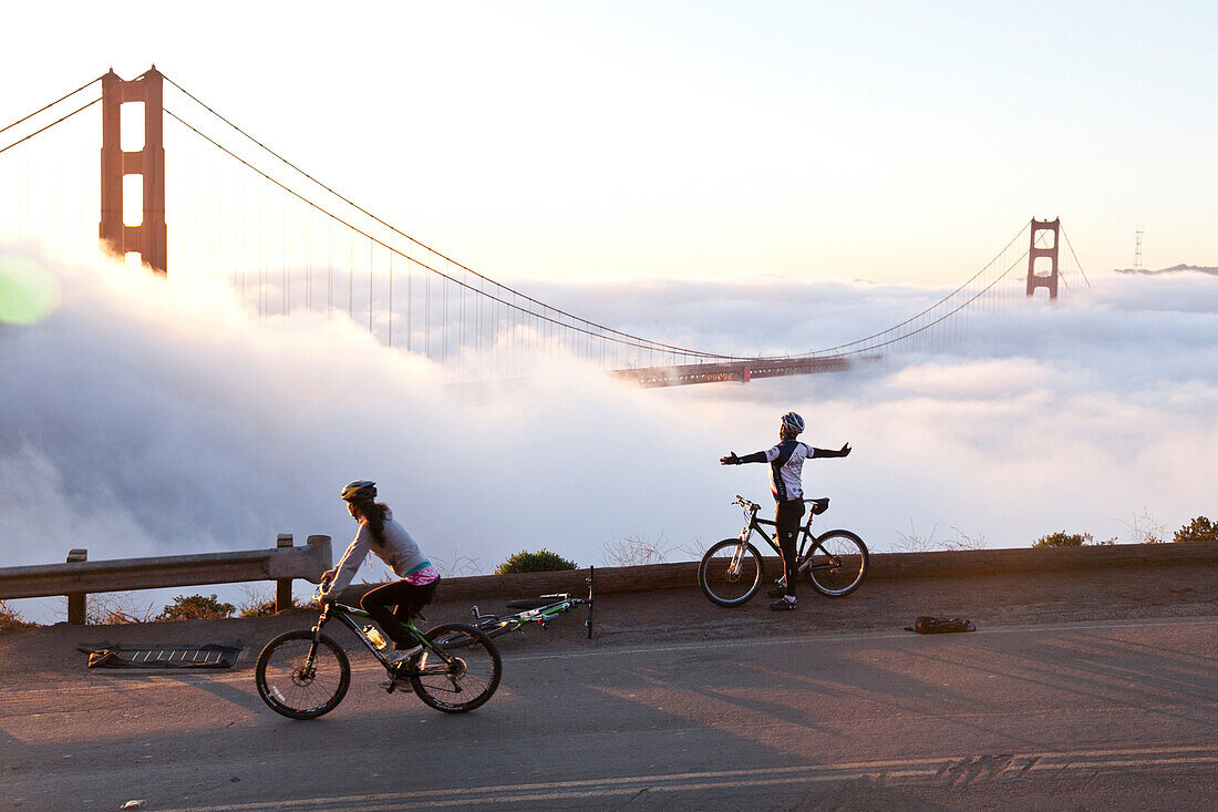 Fahrradfahrer, ausgebreitete Arme, Golden Gate Bridge in Wolken, Morgennebel, Symbol von San Francisco und Kalifornien, San Francisco, Kalifornien, Vereinigte Staaten von Amerika, USA