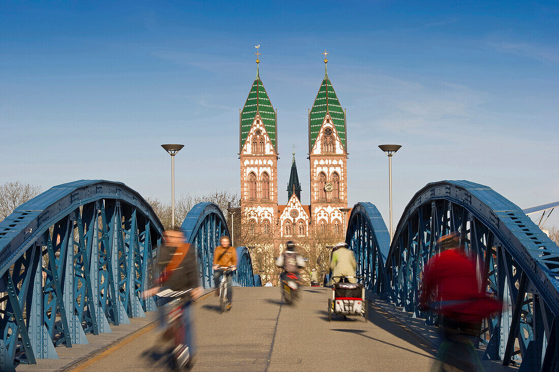 Cyclists passing Wiwili bridge, Church of the Sacred Heart in background, Freiburg im Breisgau, Baden-Wurttemberg, Germany