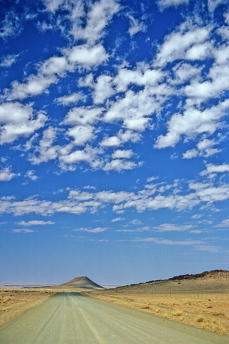 Desert road in Namibia, blue skies and dry arid grass scrub land in foreground, Namibia