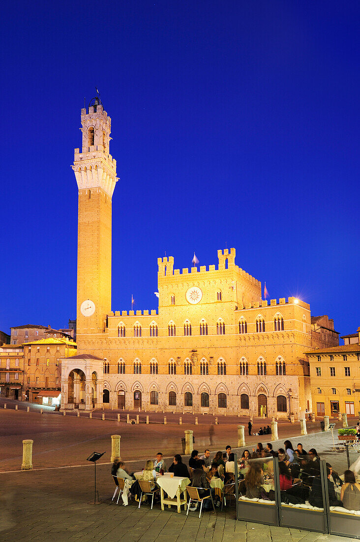 Personen sitzen in Straßenrestaurant am beleuchteten Hauptplatz Piazza del Campo von Siena mit Torre del Mangia im Hintergrund, Siena, UNESCO Weltkulturerbe Siena, Toskana, Italien