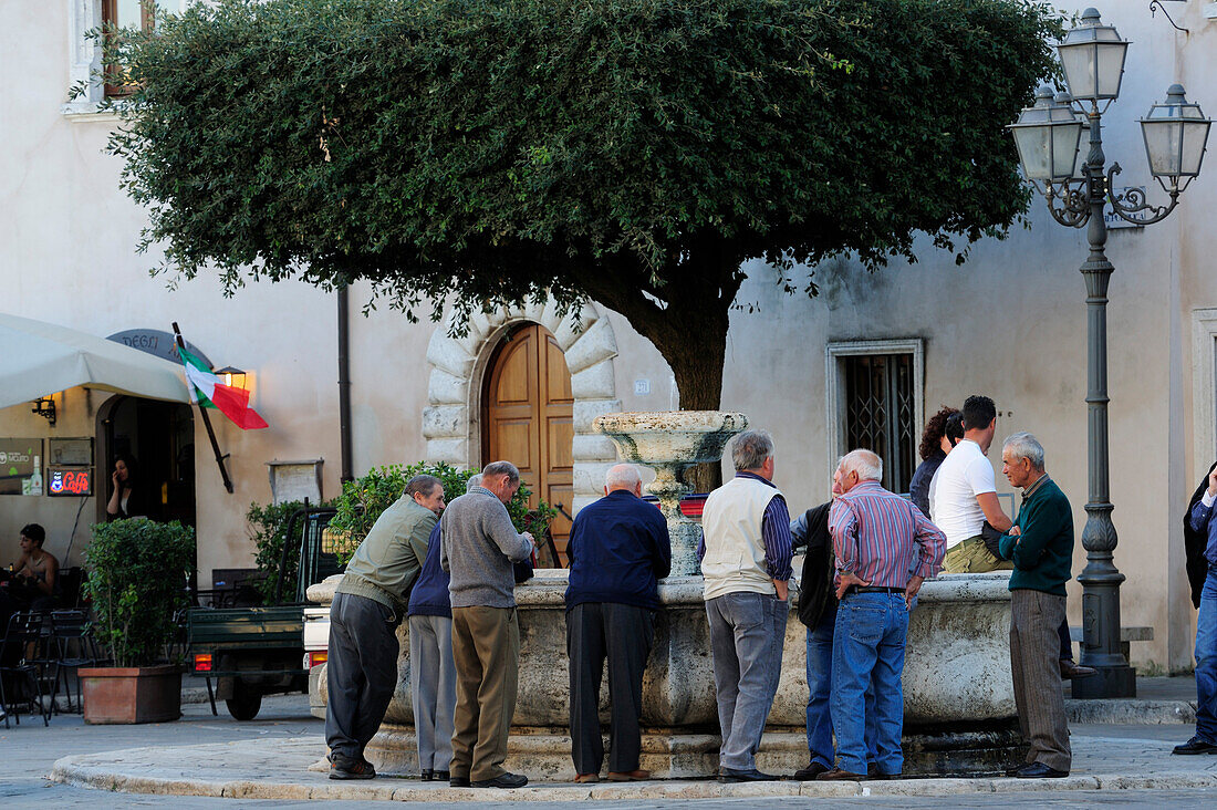 Männer stehen um Dorfbrunnen und unterhalten sich, Pitigliano, Toskana, Italien