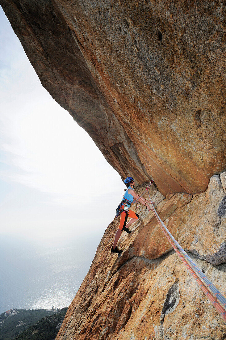 Frau klettert unter Felsüberhang, Monte San Bartolomeo, Chiessi, Insel Elba, Toskana, Italien