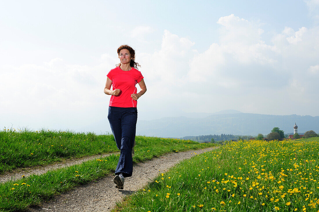 Woman jogging along a path through a meadow, Upper Bavaria, Bavaria, Germany