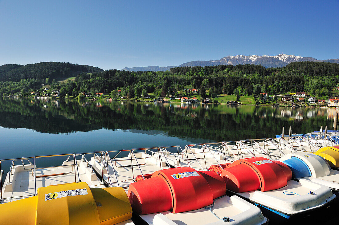 Multicolored pedal boats at lake Millstaetter See with snow covered mountains in the background, Seeboden, lake Millstaetter See, Carinthia, Austria, Europe