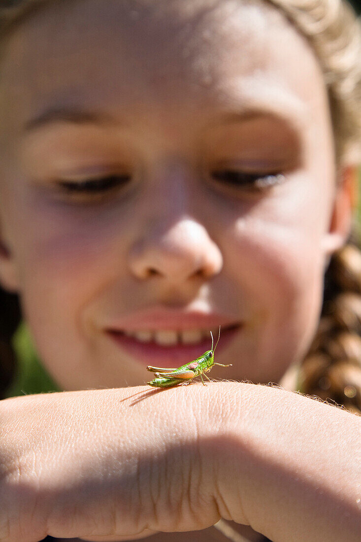 Mädchen (8 Jahre) mit einer Heuschrecke auf dem Handrücken, Bayern, Deutschland