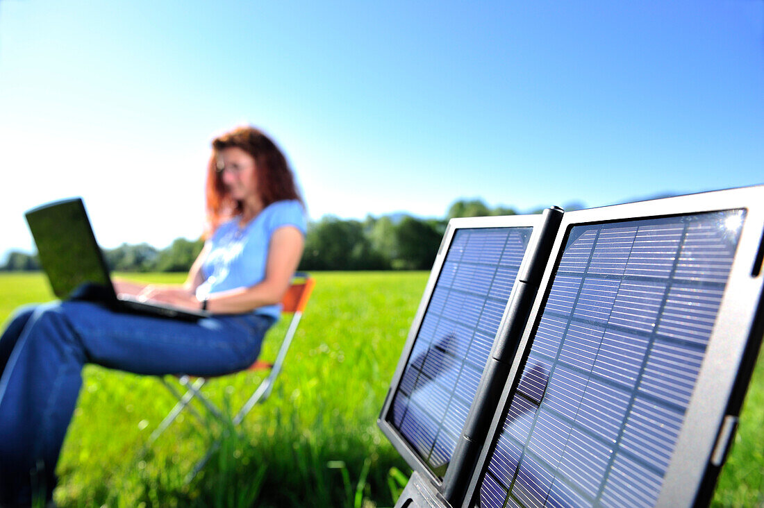 Solar panel producing electricity, woman with laptop out of focus in background, Bavaria, Germany