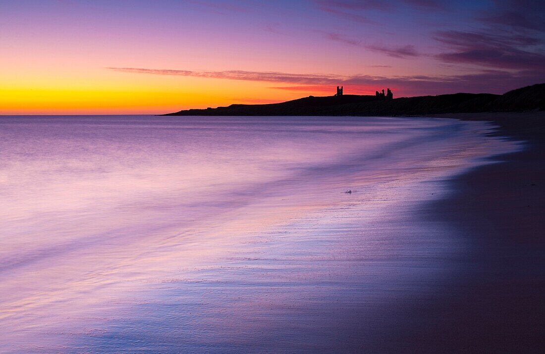 England, Northumberland, Embleton Bay A colourful display of pre-dawn colours relected upon the wet sands of Embleton Bay, overlooked by the dramatic ruins of Dunstanburgh Castle
