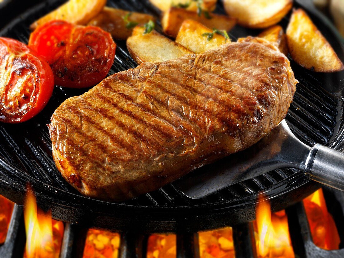 Sirloin beef steaks, tomatoes & chips being pan fried on a bbq