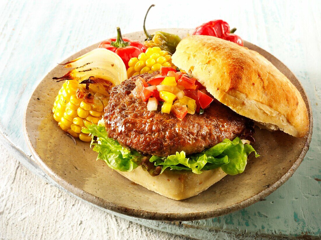 BBQ beef burger in a chabatta roll with salsa & BBQ vegetables on a rustic plate