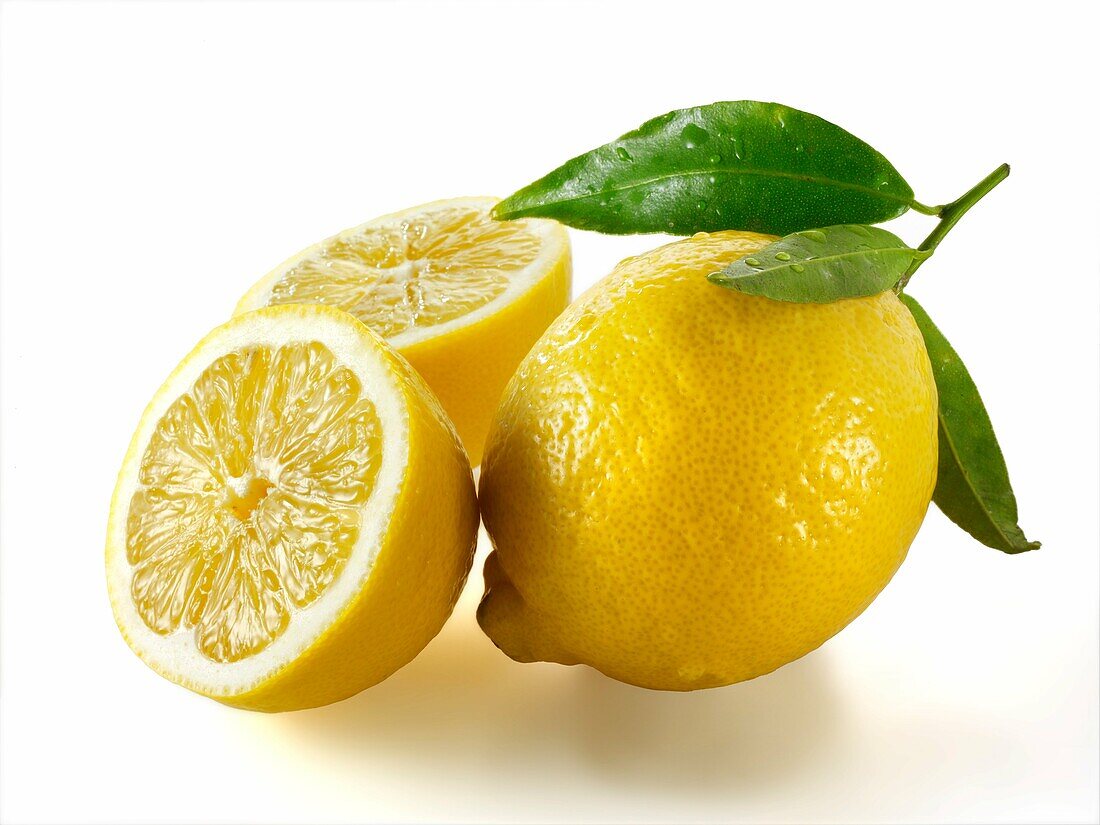 Fresh whole and cut lemons with leaves