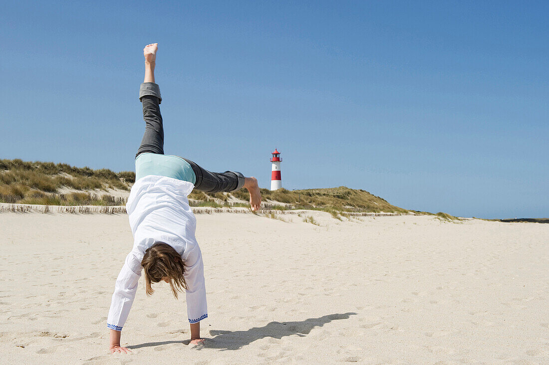 Woman turning cartwheels on sandy beach, Ellenbogen, List, Sylt, Schleswig-Holstein, Germany