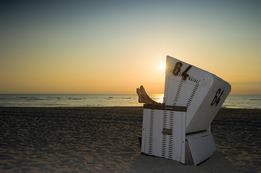 Woman relaxing in roofed wicker beach chair in sunset, Westerland, Sylt, Schleswig-Holstein, Germany
