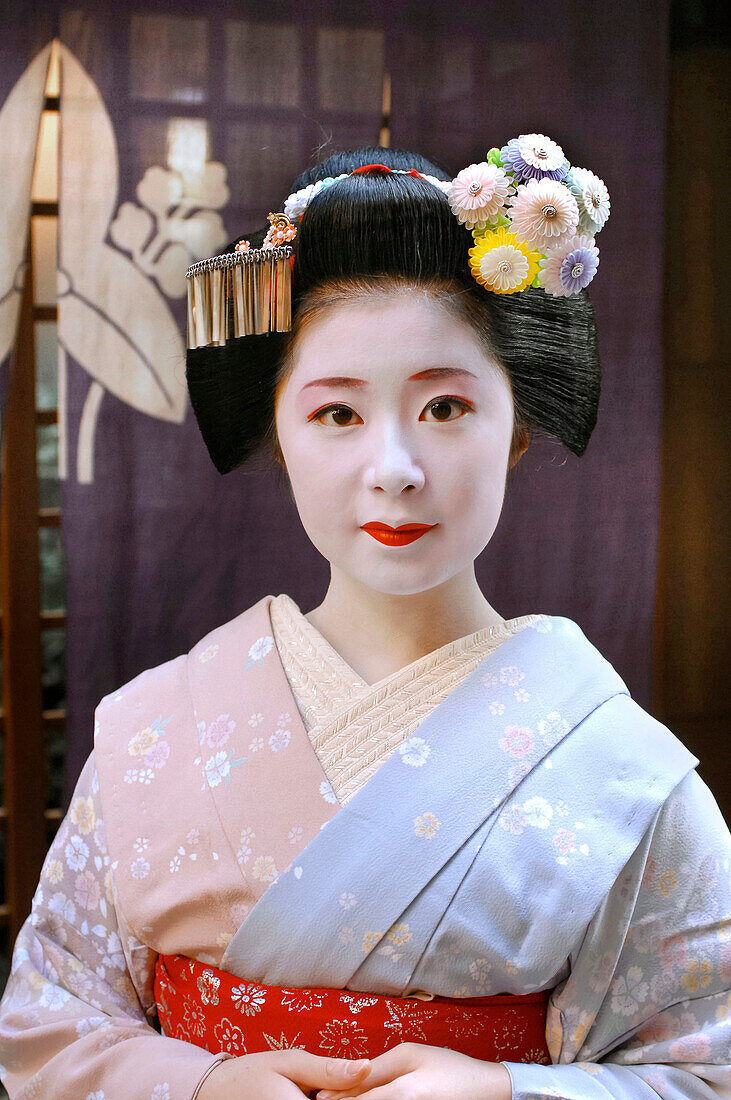 Portrait of a Maiko (Apprentice Geisha) in a Kimono (Obede), and Wearing a Chignon High on Her Head in the Form of a Peach (Wareshinobu) Adorned with a Red Silk Ribbon(Kanoko), a Decorated Hairpin (Kanzashi) and a Bouquet of Flowers (Hanakanzashi), and Ma