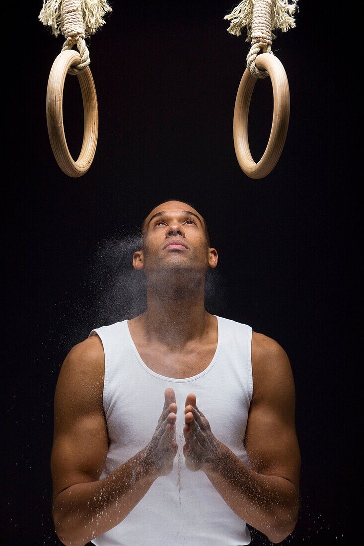 Gymnast man powdering hands on rings.