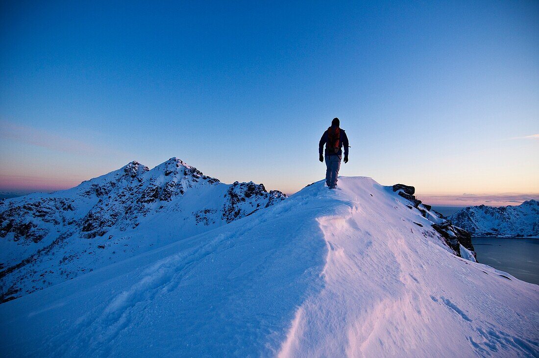 Person hikes along snow covered ridge of Stamsundheia with Steinstind peak in distance, Stamsund, Vestvågøy, Lofoten islands, Norway