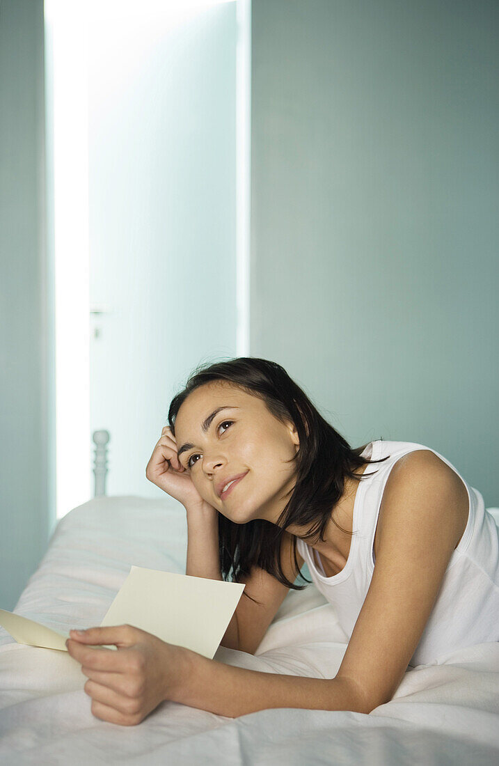 Woman lying on bed with letter, daydreaming