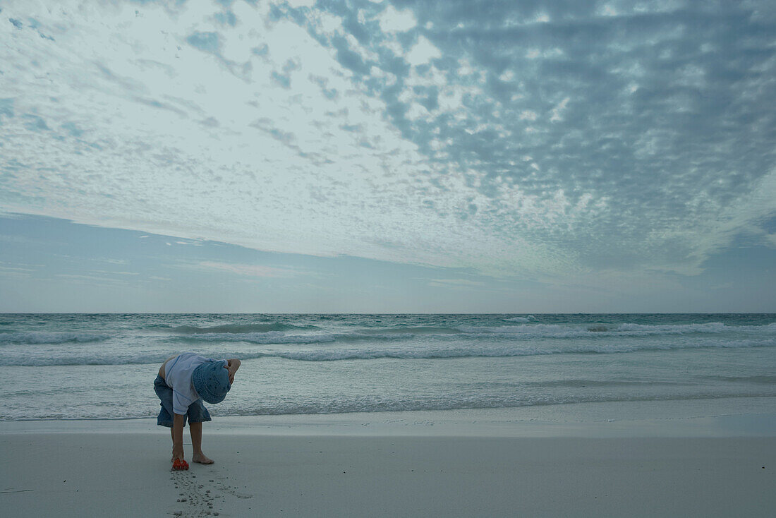 Boy bending over on beach, making lines in sand