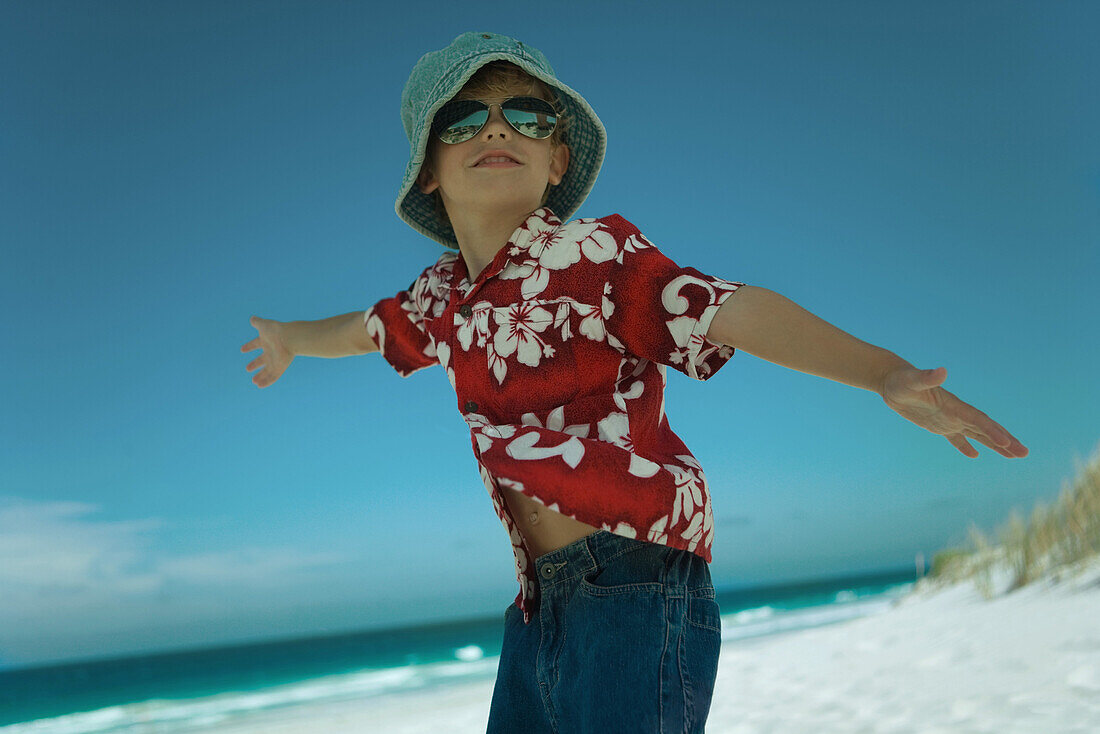 Boy standing on beach, wearing beach clothes and hat