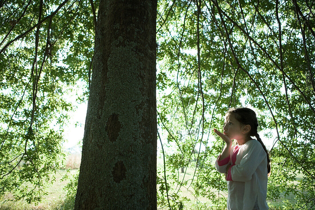 Girl standing under tree, blowing kiss, side view
