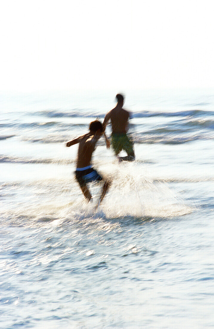 Man and boy playing in waves at beach