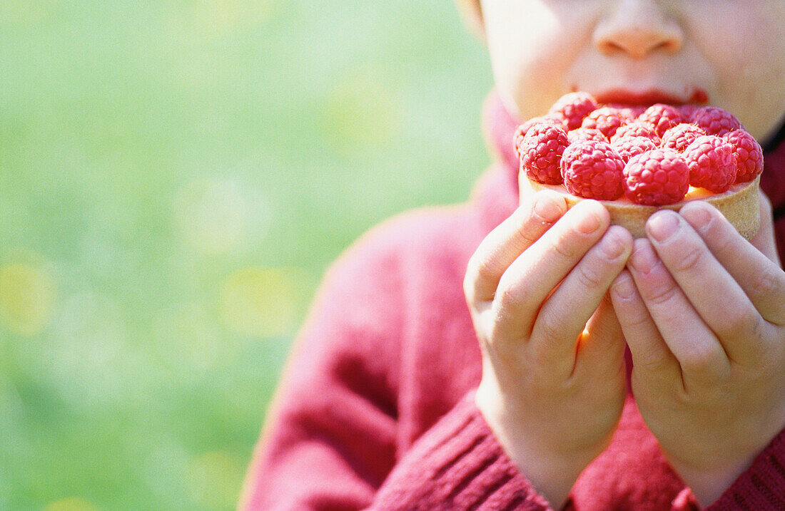Child holding raspberry tartlette in front of mouth