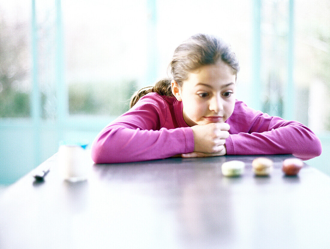 Girl sitting with head on table, looking at three cookies