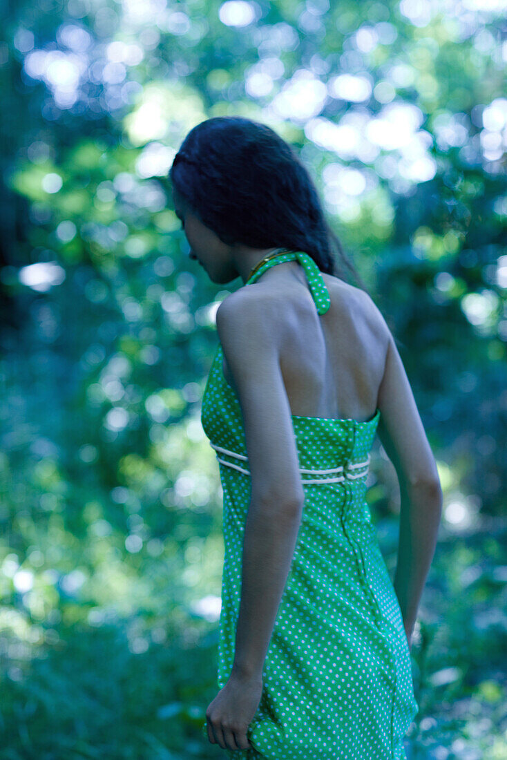 Rear view of a young woman walking through forest, wearing sundress, selective focus