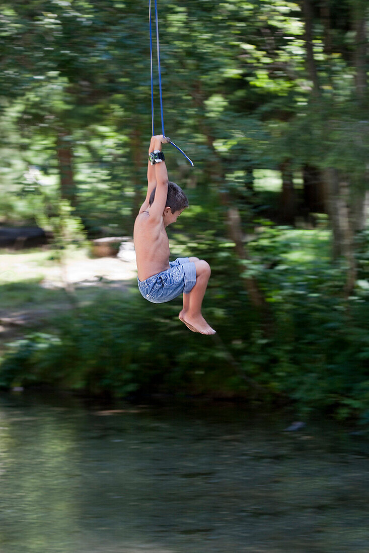 Young Boy Swinging on Rope Swing Over Stream
