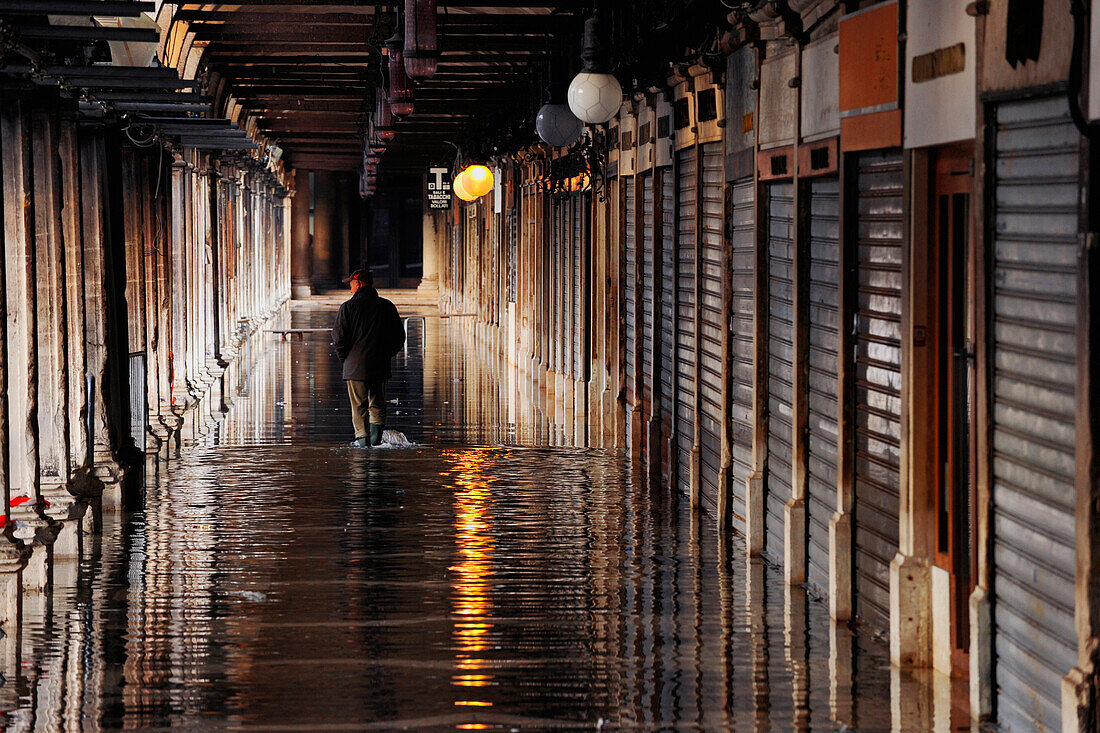Lonely man goes along alley, Reflection, flood water, Aqua Alta, arcades, Piazza San Marco, Venice, Italy