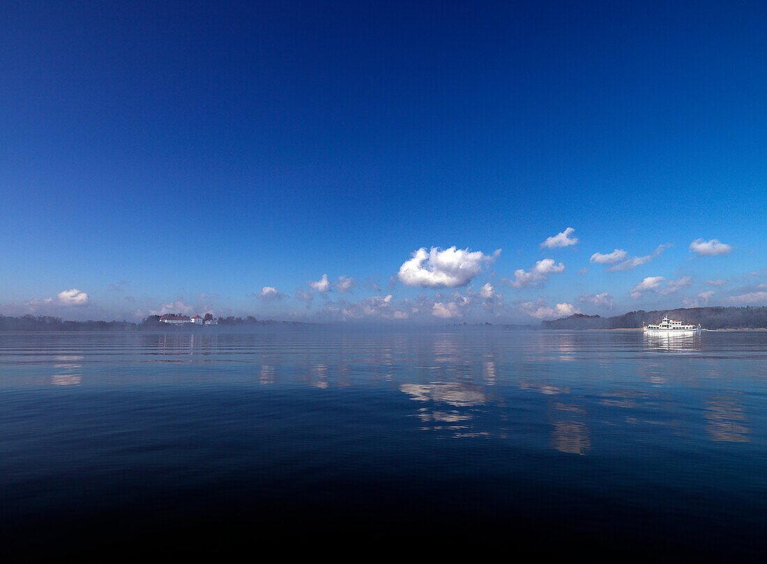 View across the reflecting lake towards Herreninsel, ferry boat, Lake Chiemsee, Chiemgau, Bavaria, Germany