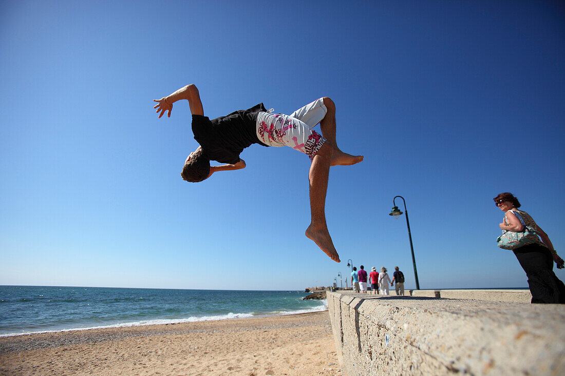 Junger Mann springt von Hafenmauer am Castillo de San Sebastian, Calle de Fernando Quiñones, Cadiz, Provinz Cadiz, Andalusien, Spanien