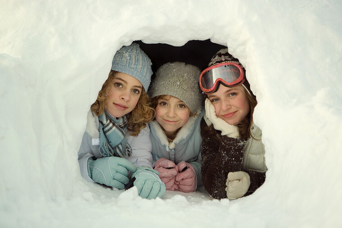 Three young friends lying in snow tunnel, smiling at camera