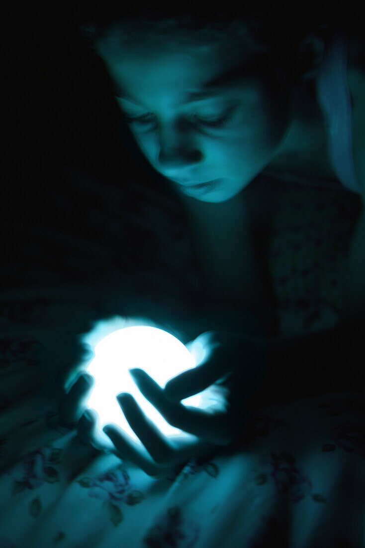 Female in the dark holding glowing sphere, looking down, close-up