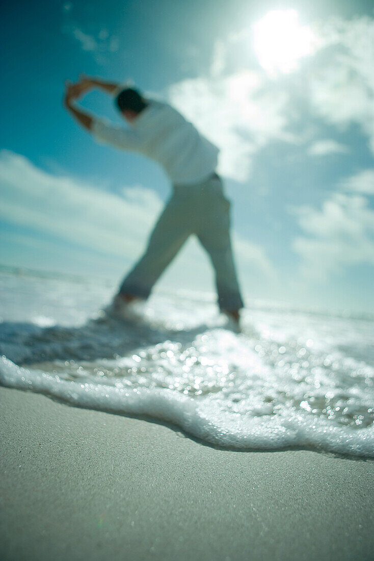 Man standing at the beach with arms raised, low angle rear view