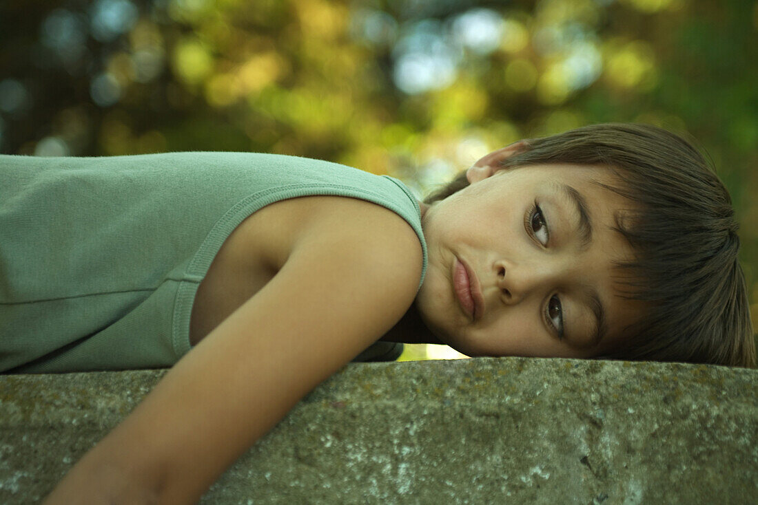 Little boy lying on stomach outdoors, frowning, looking away
