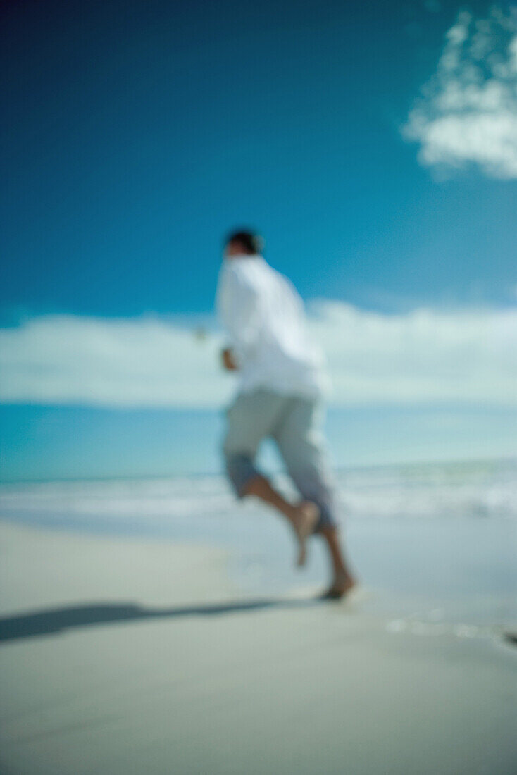 Man running at the beach, rear view, defocused