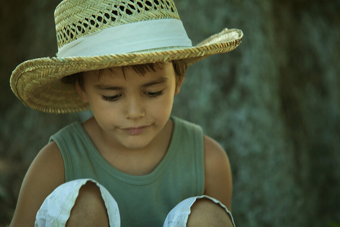 Little boy wearing straw hat, looking down, close-up