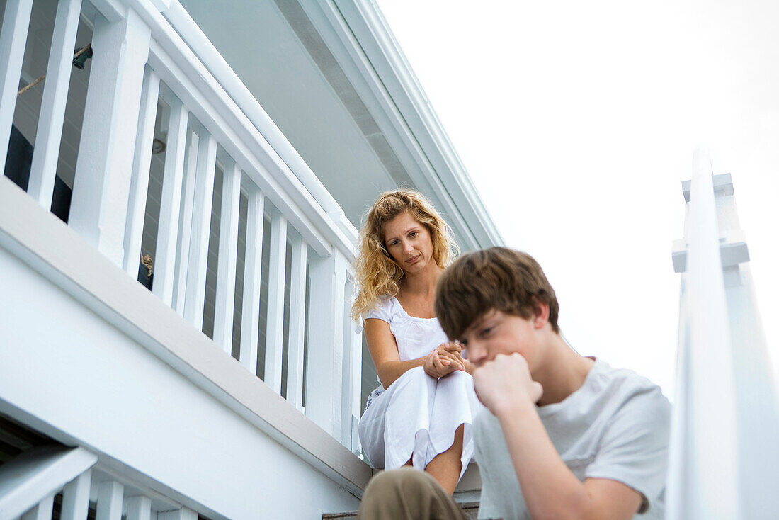 Mother and teenage son sitting on steps, son sulking