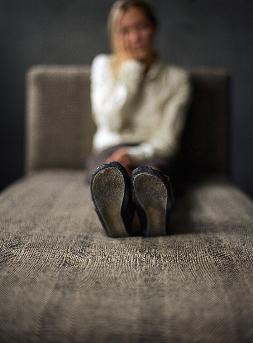Young woman sitting on divan, holding head, focus on sole of shoes