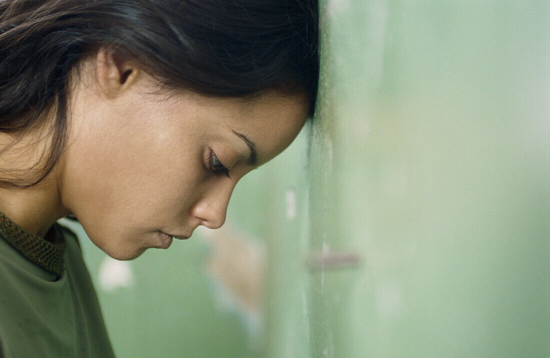 Young woman pressing her head against a wall, profile