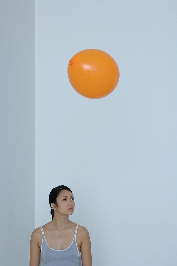 Orange balloon floating over woman's head, woman looking away