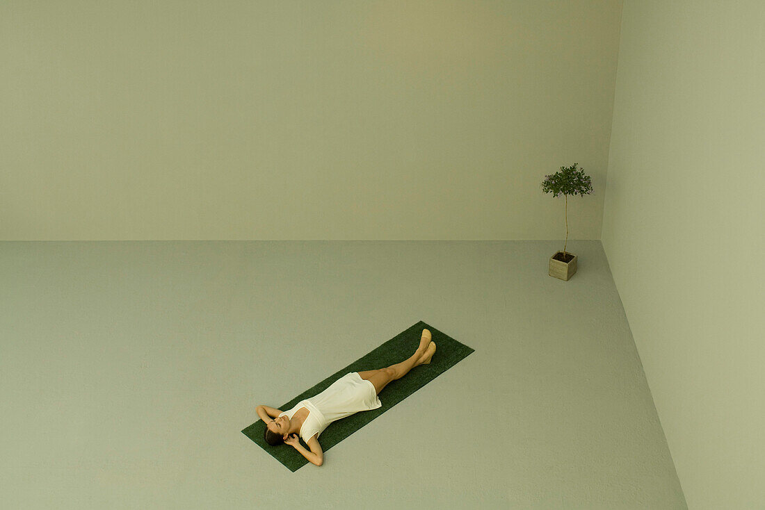 Woman lying on back on artificial turf, potted plant nearby, high angle view