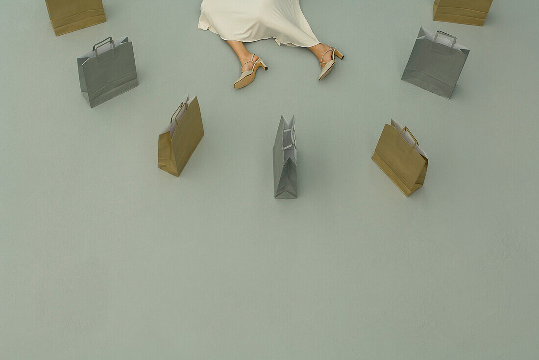 Woman lying on the ground, surrounded by shopping bags, cropped view