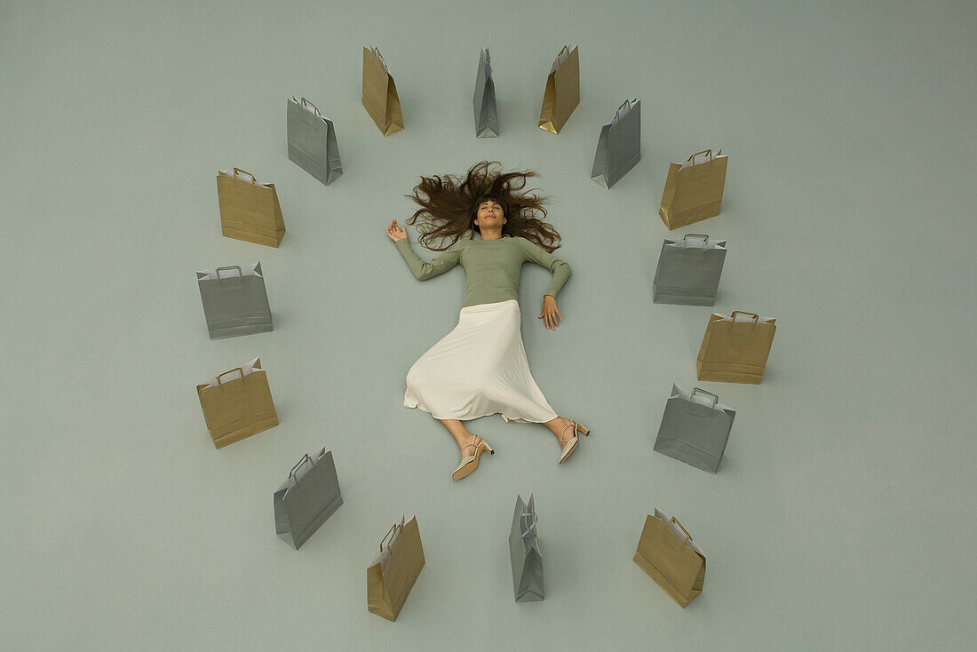 Woman lying on the ground, surrounded by shopping bags, overhead view