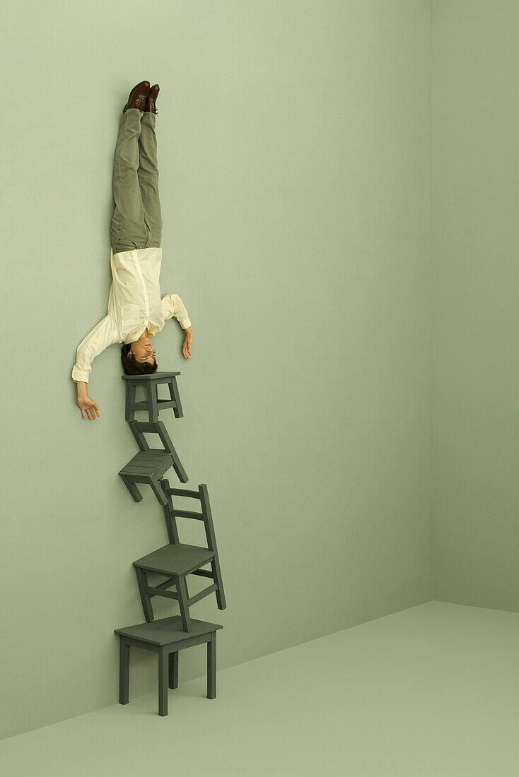 Man doing headstand on top of tall stack of chairs