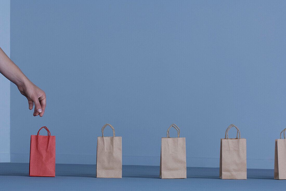 Paper gift bags in a row, woman's hand reaching for solitary red bag